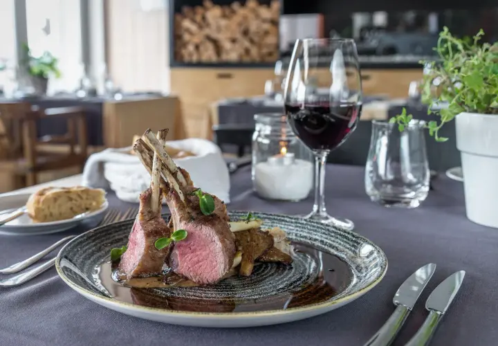 Carré d'agnello al forno con funghi e un bicchiere di vino rosso, un abbinamento perfetto per un pasto speciale.