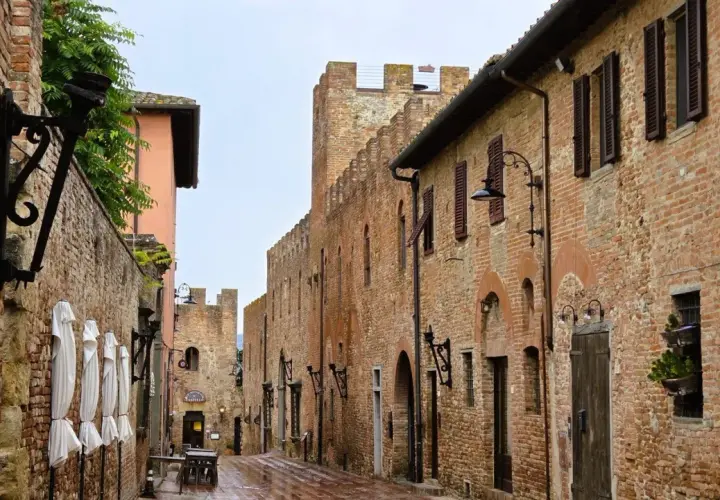Vicoli medievali di Certaldo cosa vedere: un'antica strada in mattoni con torri merlate, lampioni in ferro battuto e finestre con persiane.