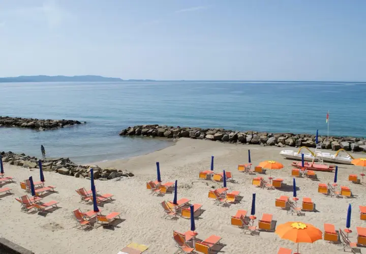 Spiaggia attrezzata con lettini e ombrelloni arancioni, mare azzurro e scogli. Un sogno di vacanza a Pratoranieri Follonica.