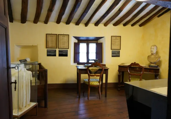 Interno di una casa museo, con travi a vista, una scrivania con macchina da cucire, un busto e un abito in esposizione. Un luogo dove le case della memoria prendono vita.
