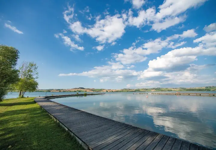 Passerella in legno su un lago tranquillo, con colline ondulate sullo sfondo. Un luogo idilliaco in Valdichiana, dove la natura incontra la serenità.