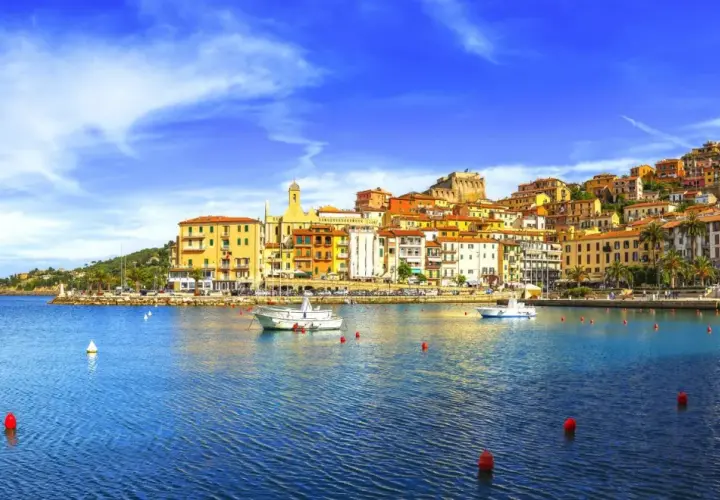 Vista del porto di Porto Santo Stefano, con case colorate che si arrampicano sulla collina e barche sull'acqua blu.