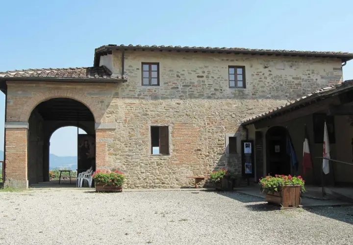 La casa di Giotto, un edificio in pietra con un grande arco, fiori rossi e bandiere.
