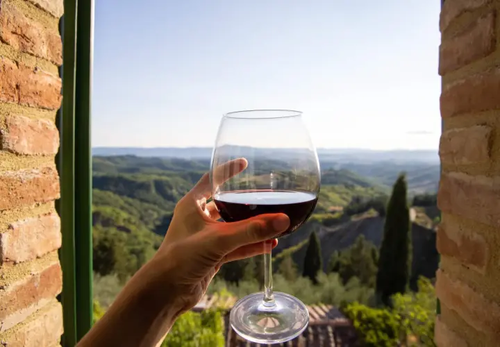 Un bicchiere di vino rosso, con il paesaggio del Val d'Orcia sullo sfondo. Un momento di puro piacere.