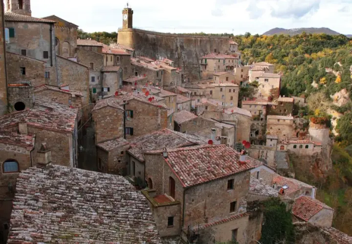 Sorano, Toscana: un borgo medievale arroccato su una rupe tufacea, con tetti rossi e case in pietra che si fondono con il paesaggio autunnale.