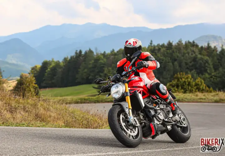 Motociclista in tuta rossa affronta una curva sul passo del giogo, con montagne sullo sfondo.