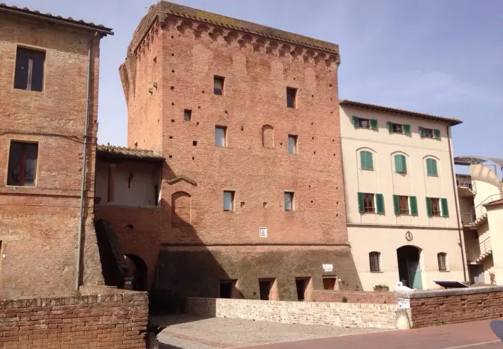 Torre medievale in mattoni a Monteroni d'Arbia, con edifici adiacenti in pietra e intonaco.