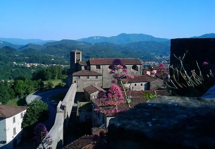 Panoramica di Castiglione di Garfagnana con il suo castello, le case con i tetti rossi e le montagne verdi sullo sfondo.