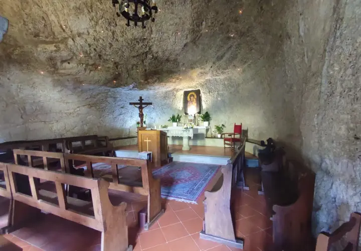 Interno dell'eremo di Calomini, con panche in legno, altare, crocifisso e un'icona sacra incastonati nella roccia.
