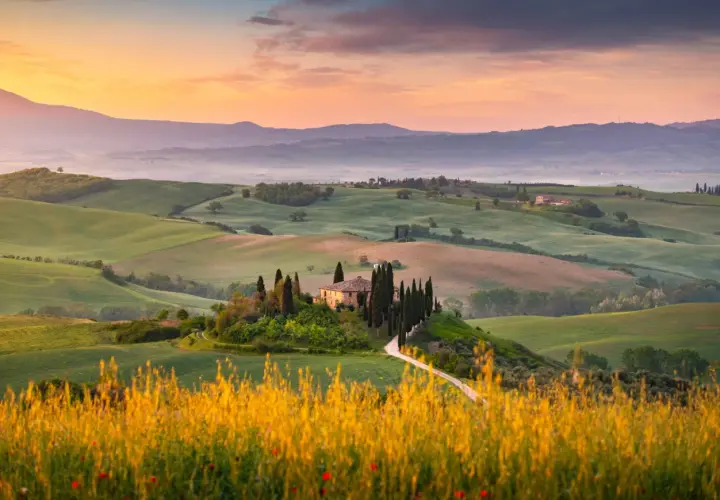 Dolci colline verdi nel Val d'Orcia, con una casa colonica e cipressi su una collina, al tramonto.