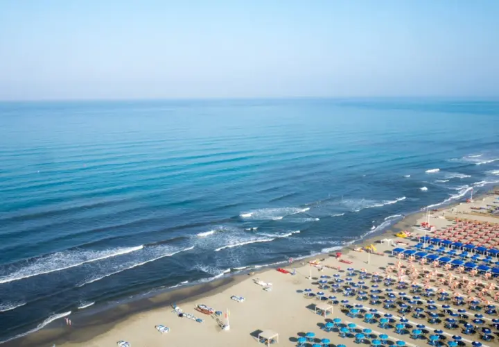 Ampia spiaggia attrezzata al **Lido di Camaiore**, con file ordinate di ombrelloni blu e arancioni che si estendono verso il mare calmo e azzurro.