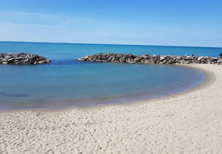 Spiaggia di Marina di Pisa con acque calme e dighe frangiflutti in pietra.