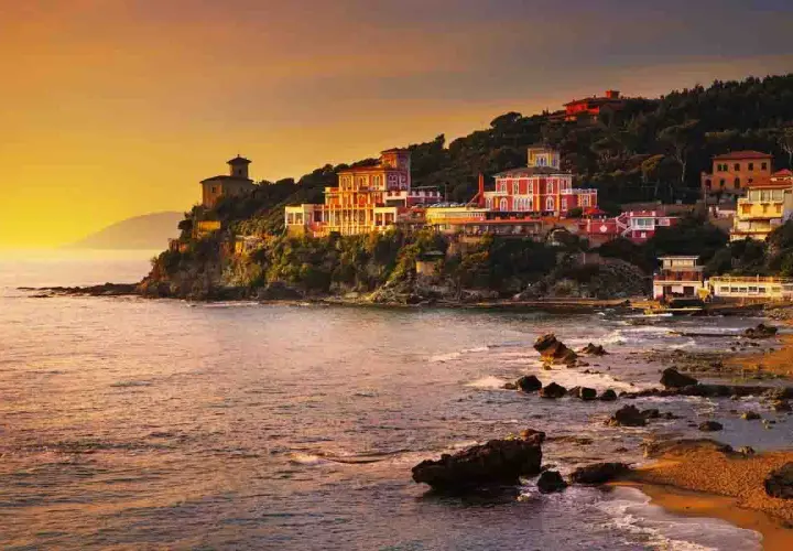 Ville colorate aggrappate alla scogliera, con il mare che lambisce la costa rocciosa. Un tramonto dorato illumina i borghi vicino Castiglioncello.