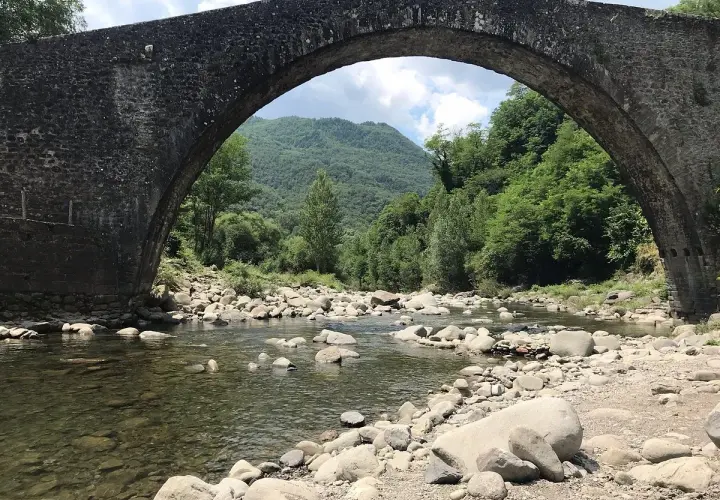 Il ponte di Castruccio, con il suo arco maestoso, sovrasta un fiume serpeggiante tra rocce e vegetazione lussureggiante.