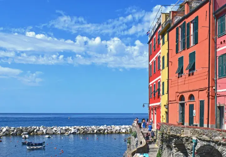 Case, a Firenze c'è il mare! Case colorate affacciate su un porto con barche, sotto un cielo azzurro con nuvole bianche.