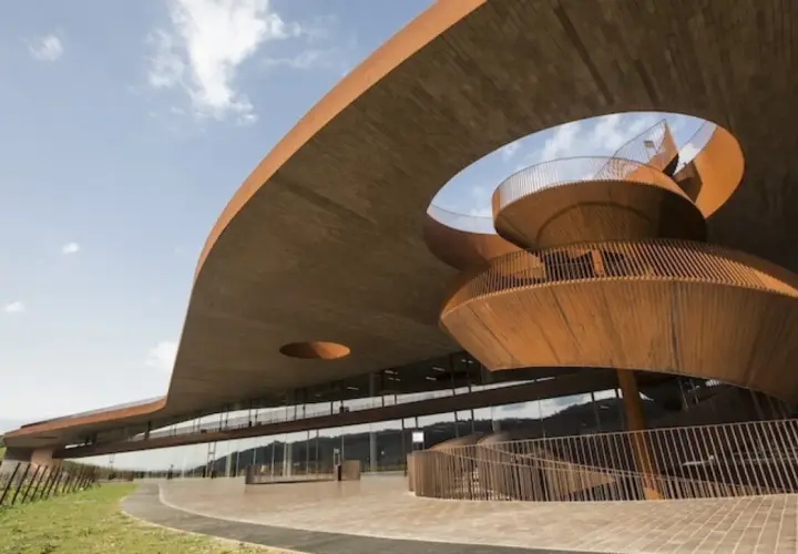 Edificio moderno con scala a chiocciola in legno, probabile la **best winery in Tuscany**, immersa nel verde.