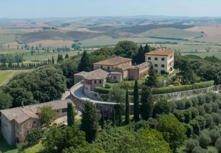 Un borgo toscano con casali in pietra e un edificio giallo, immerso nel verde e con dolci colline sullo sfondo. Castelnuovo Tancredi, un'oasi di pace.
