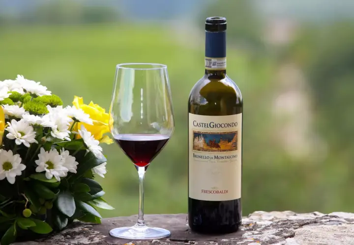 Un bicchiere di Brunello di Montalcino, un vino pregiato, accanto a un bouquet di fiori e una bottiglia CastelGiocondo.