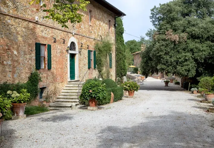 Ingresso della fattoria del colle Trequanda, con scalinata in pietra, porta verde e piante in vaso.