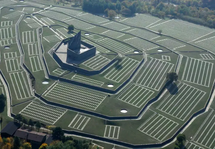 Vasta distesa di tombe bianche disposte in file ordinate, con un imponente monumento centrale. Il cimitero tedesco del Passo della Futa, un luogo di memoria.