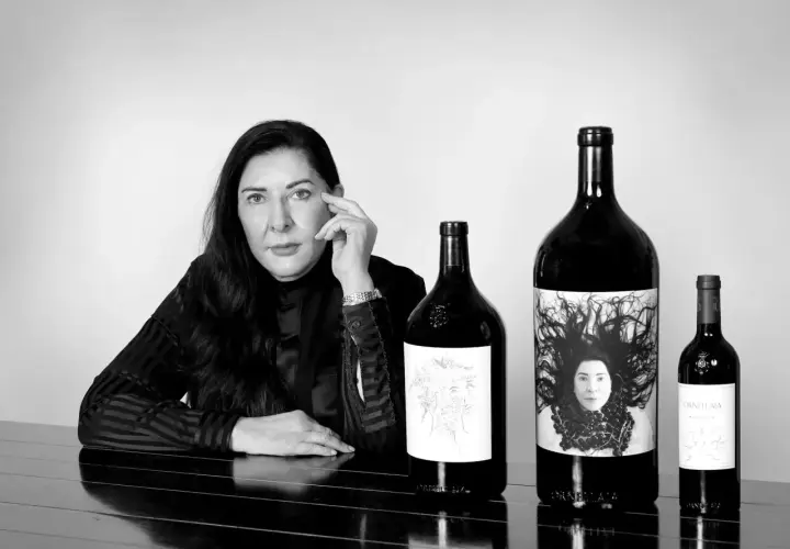 Donna con le migliori annate Ornellaia. Le bottiglie presentano etichette artistiche, una con un ritratto.
