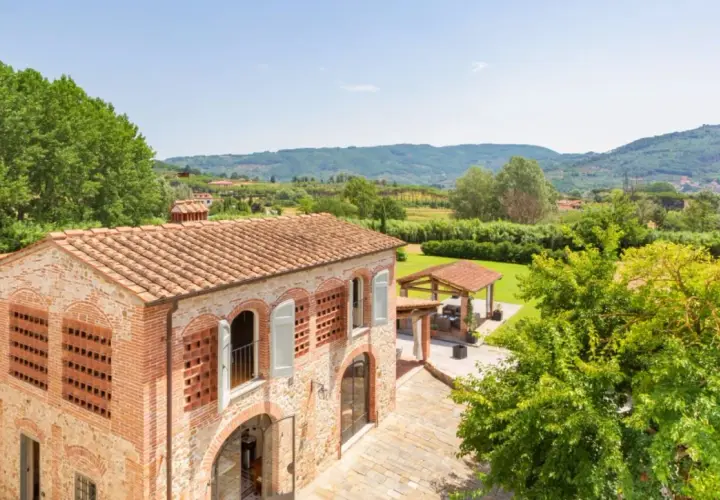 Antica pieve a Nievole con tetto in cotto, circondata da verde lussureggiante e colline toscane.
