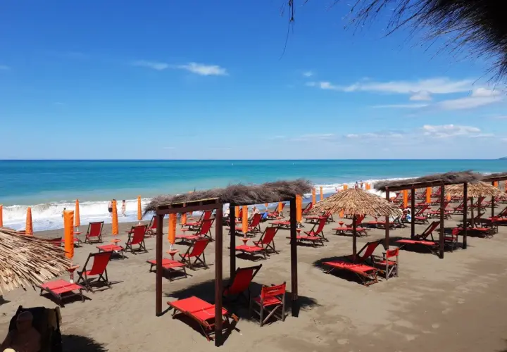 Marina di Bibbona spiagge più belle: lettini rossi e ombrelloni di paglia sotto un cielo azzurro, con il mare calmo all'orizzonte.