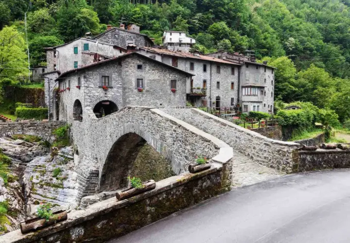 Ponte in pietra a Vergemoli, con case in pietra e vegetazione lussureggiante sullo sfondo. Le fabbriche di Vergemoli sembrano immerse nella natura.