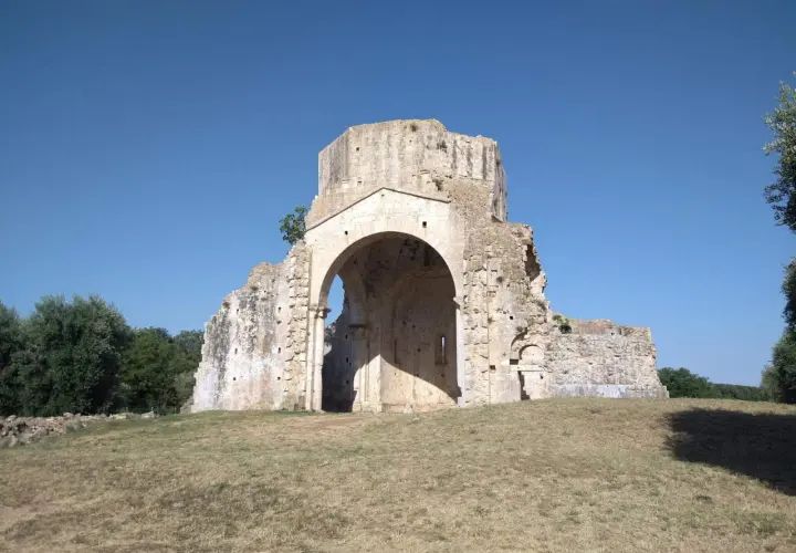 Rovine dell'abbazia di San Bruzio sotto un cielo azzurro, con alberi sullo sfondo.