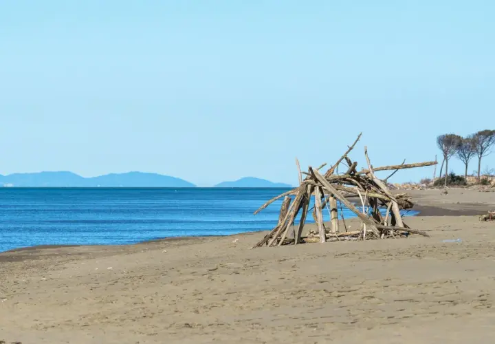 Spiaggia del Parco dell'Uccellina con un rifugio di legni sulla sabbia e il mare blu all'orizzonte.