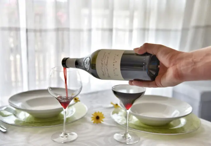 Versare vino rosso in un calice, un passo fondamentale per capire come si fa il vino rosso. La tavola è apparecchiata.