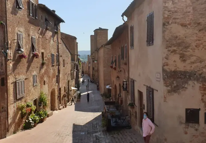Un vicolo medievale a Certaldo, dove si trova il borgo antico con case in mattoni, finestre con persiane e fiori.