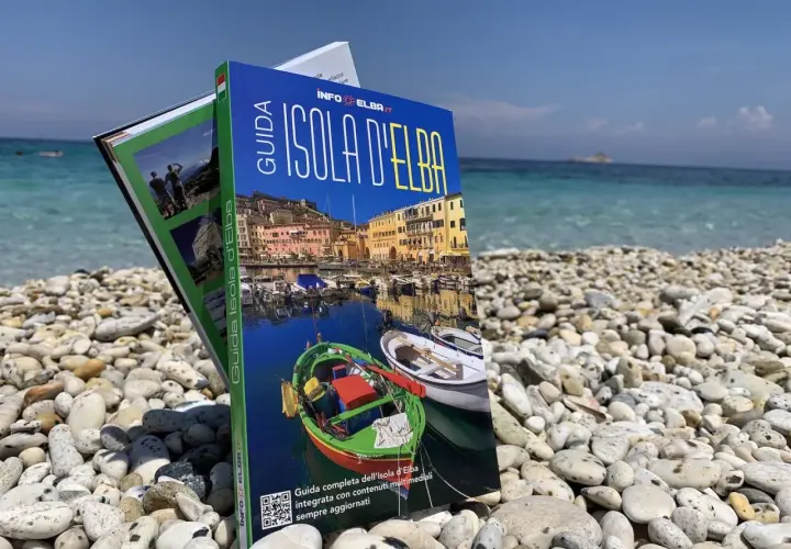 Guida turistica "Isola d'Elba" su una spiaggia di ciottoli, con il mare azzurro sullo sfondo. Perfetta per pianificare la tua vacanza.