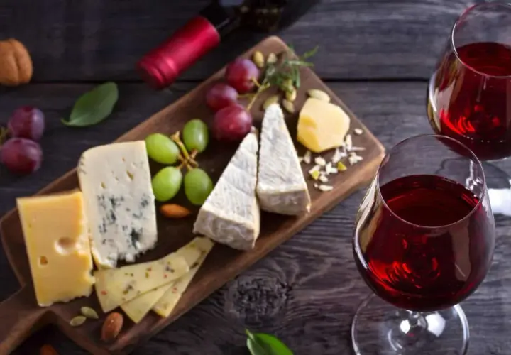 Un tagliere di formaggi misti, uva e frutta secca, perfetto per i rosso di Montalcino abbinamenti. Due calici di vino rosso completano la scena.