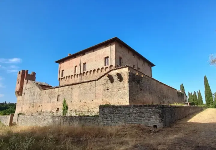 Rocche e mura antiche a Civitella Paganico cosa vedere: un castello medievale in mattoni rossi sotto un cielo azzurro, circondato da vegetazione rigogliosa.