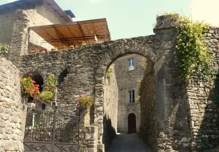 Un vicolo suggestivo a Casola in Lunigiana, con un arco in pietra, fiori rossi e edera rampicante.