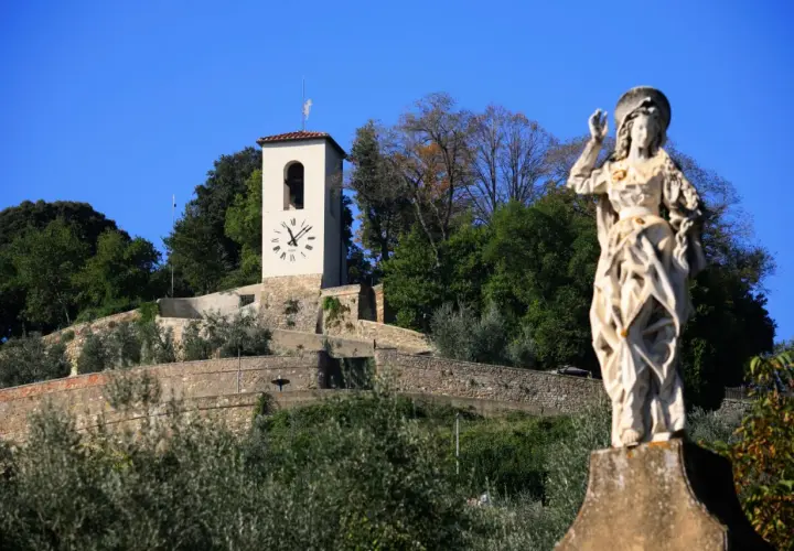 Statua di santo e torre dell'orologio su una collina verdeggiante, un'immagine che cattura l'essenza di cosa vedere ad Artimino.