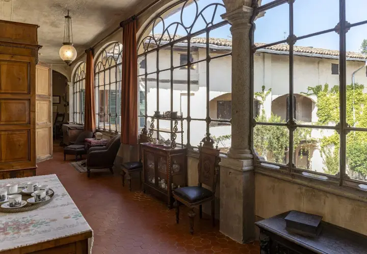 Interno elegante della villa Macchi con mobili d'epoca, grandi finestre ad arco e vista sul cortile verdeggiante.