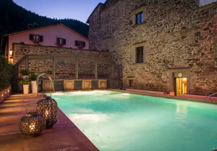 Piscina termale illuminata di notte, con cascate d'acqua e lanterne decorative. Un'oasi di relax nelle terme vicino Arezzo.