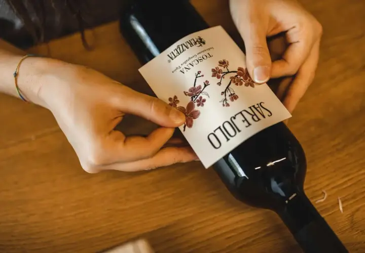 Mani che applicano l'etichetta a una bottiglia di vino rosso, forse il best wine in Tuscany.