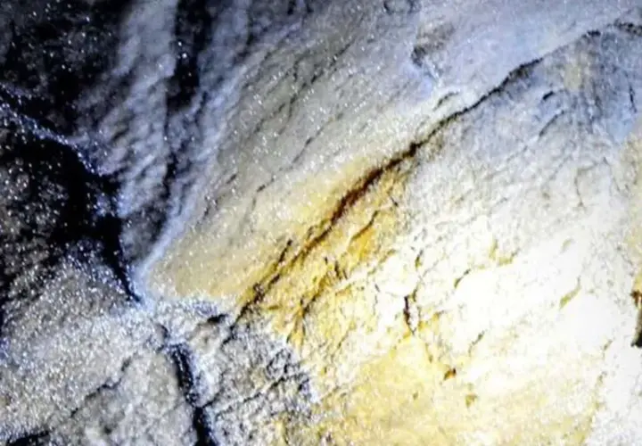Esplorazione della grotta turistica Antro del Corchia: rocce scintillanti e un casco illuminato da una torcia.