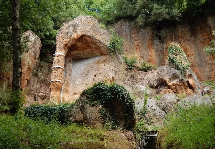 Antica tomba etrusca scavata nella roccia, con un pilastro decorato da fasce metalliche, immersa nel verde della necropoli di Sovana.