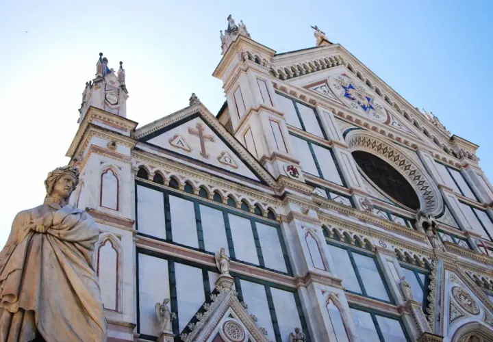 Statua di un poeta toscano davanti alla facciata in marmo di una chiesa fiorentina.