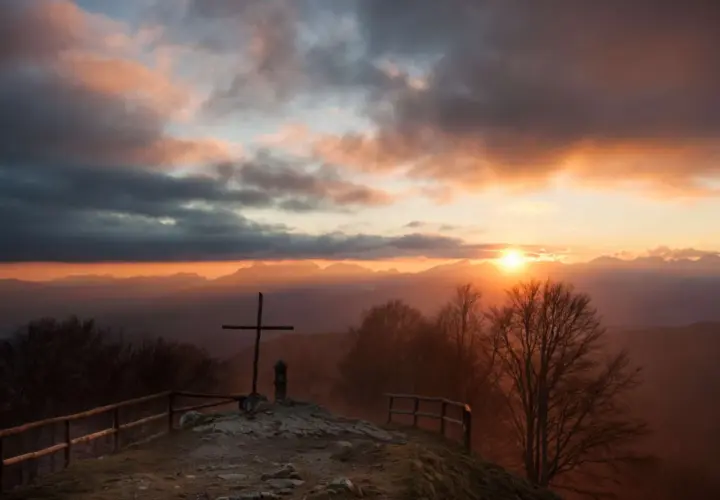 Croce in cima a una collina al tramonto, con montagne sullo sfondo. Un luogo suggestivo a San Pellegrino in Alpe.