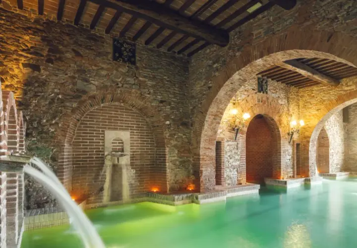 Piscina termale con archi in mattoni e pietra, cascate d'acqua e luci soffuse, un'oasi di relax nel paese di Venturina Terme.