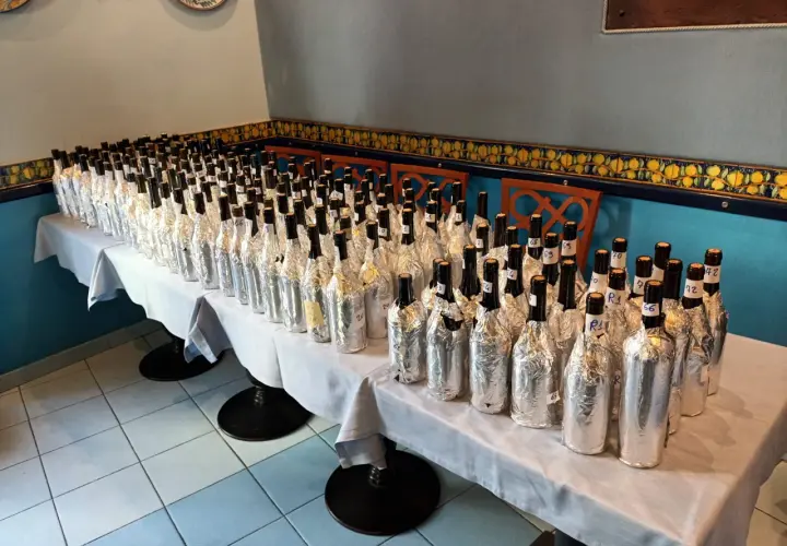 Many wine bottles wrapped in foil, lined up on a table for a tasting.