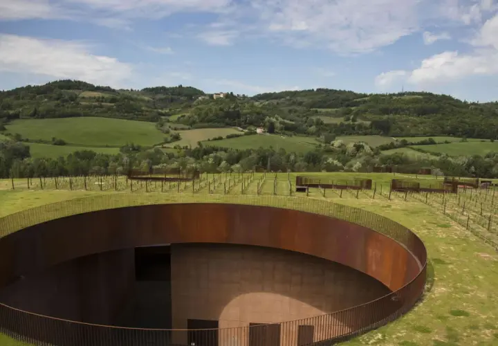 Un'avveniristica cantina toscana si fonde con il paesaggio collinare, con un tetto verde e un pozzo circolare in corten.