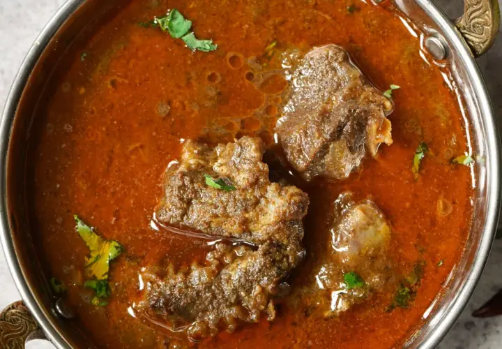 Un invitante buglione di agnello in una ciotola metallica, con pezzi di carne tenera immersi in un ricco sugo speziato e guarnito con erbe fresche.
