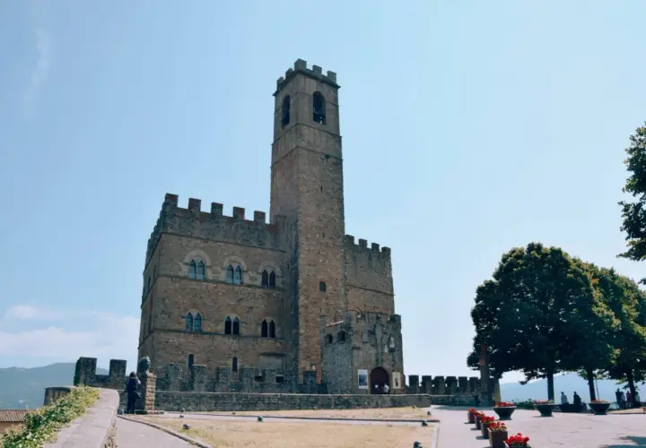 Un antico borgo alla collina domina il paesaggio, con un imponente torrione che svetta verso il cielo azzurro.