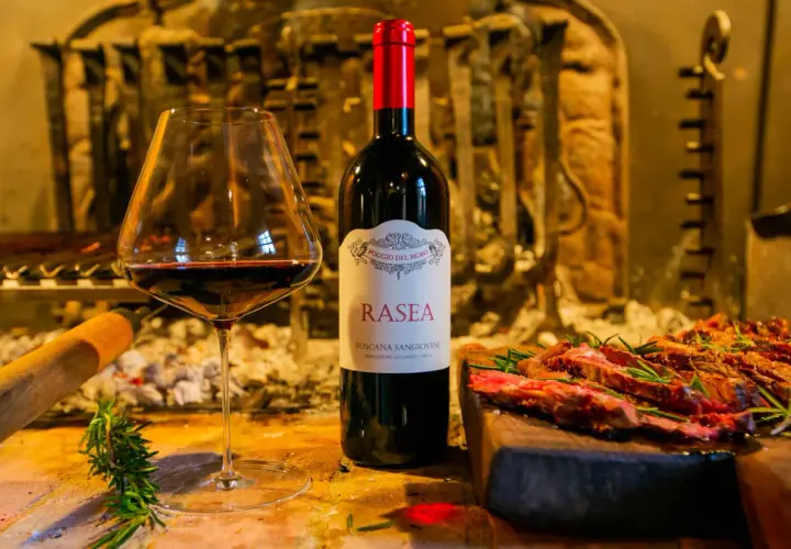 Calice di vino rosso accanto a una bottiglia di Rasea, un vino toscano, con carne grigliata e rosmarino. Un'ode ai super tuscan wines.